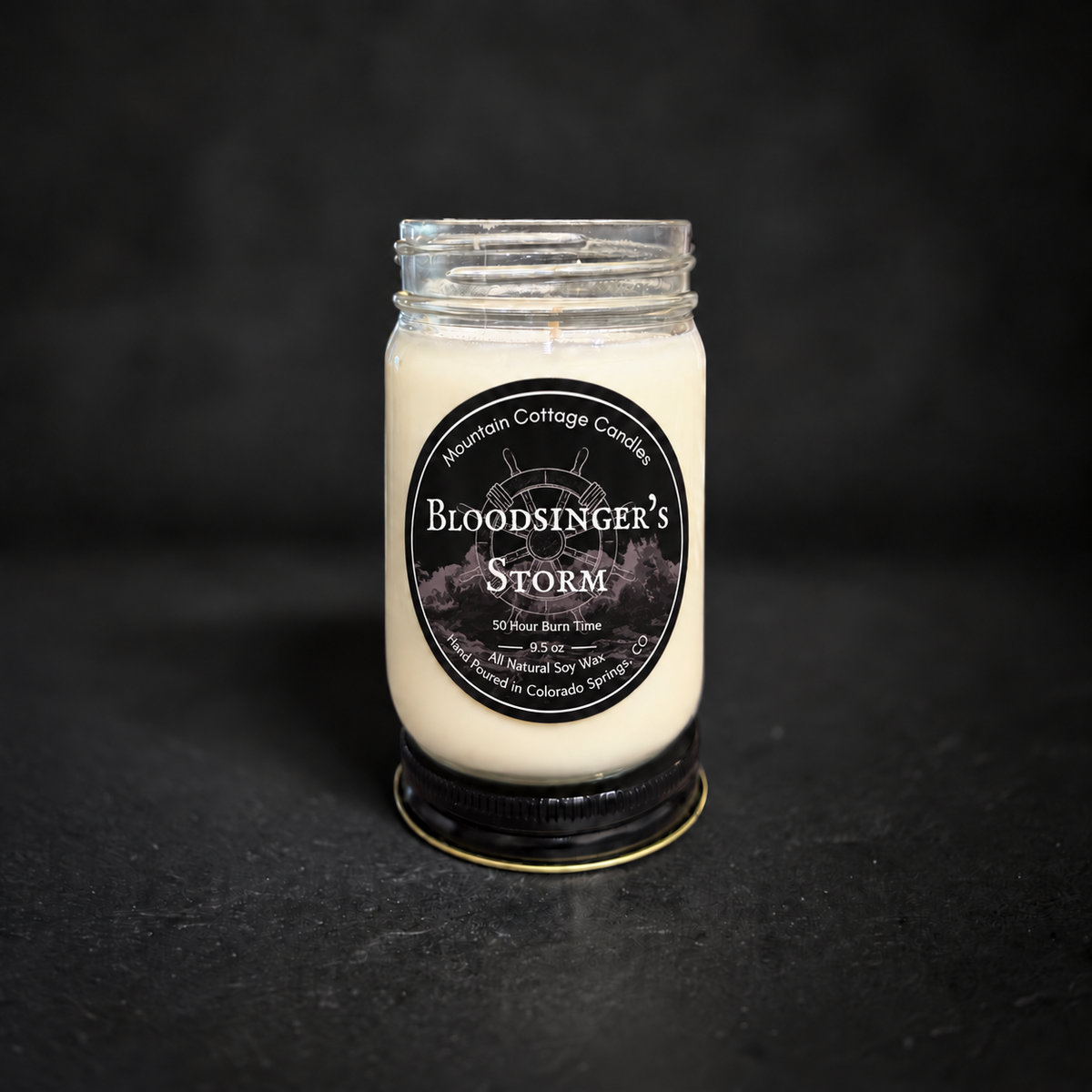 Bloodsinger's Storm soy candle in a clear glass jar with a black lid, black label with a ship's wheel above stormy waves