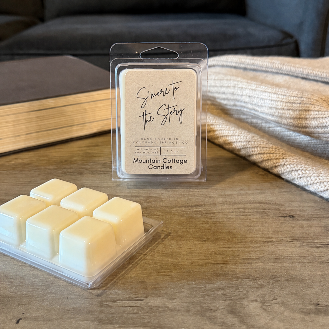 S'more to the Story soy wax melt in a kraft-labeled clamshell, six cream wax cubes laid out in front on a wood table