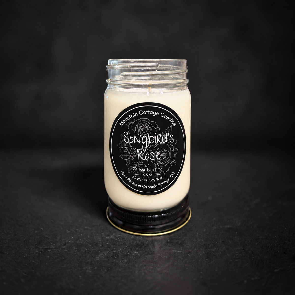 Songbird's Rose soy candle in a clear glass jar with a black lid, black label with line-drawn roses and leaves