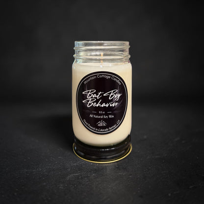 Bat Boy Behavior soy candle in a clear glass jar, black label showing faint outspread wings behind the script