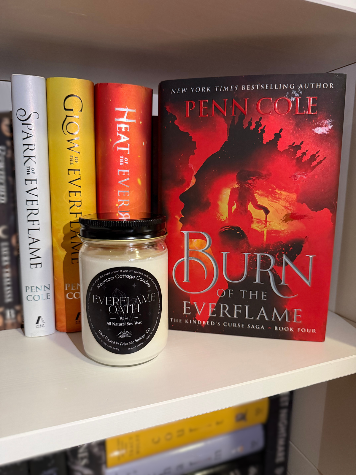 Everflame Oath soy candle on a white shelf in front of Penn Cole's Kindred's Curse Saga, Burn of the Everflame standing face out