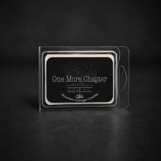 One More Chapter soy wax melt in a clear clamshell, black label showing an open book with wildflowers rising from its pages