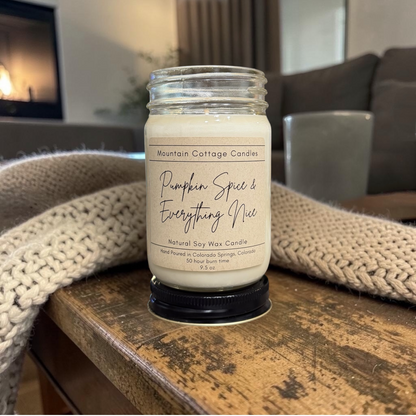 Pumpkin Spice & Everything Nice 9.5 oz soy candle in a kraft-labeled glass jar on a wood side table with a cream knit blanket behind
