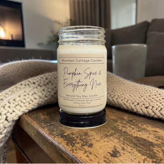 Pumpkin Spice & Everything Nice 9.5 oz soy candle in a kraft-labeled glass jar on a wood side table with a cream knit blanket behind