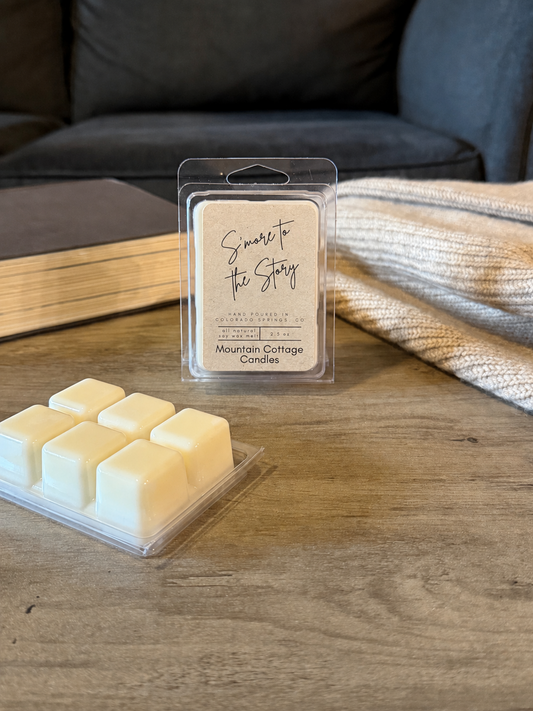 S'more to the Story soy wax melt in a kraft-labeled clamshell, six cream wax cubes laid out in front on a wood table