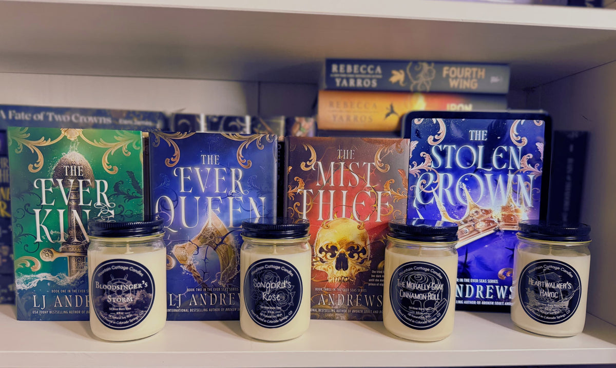 Bloodsinger's Storm, Songbird's Rose, Morally Gray Cinnamon Roll and Heartwalker's Havoc candles in front of LJ Andrews' Ever Seas books