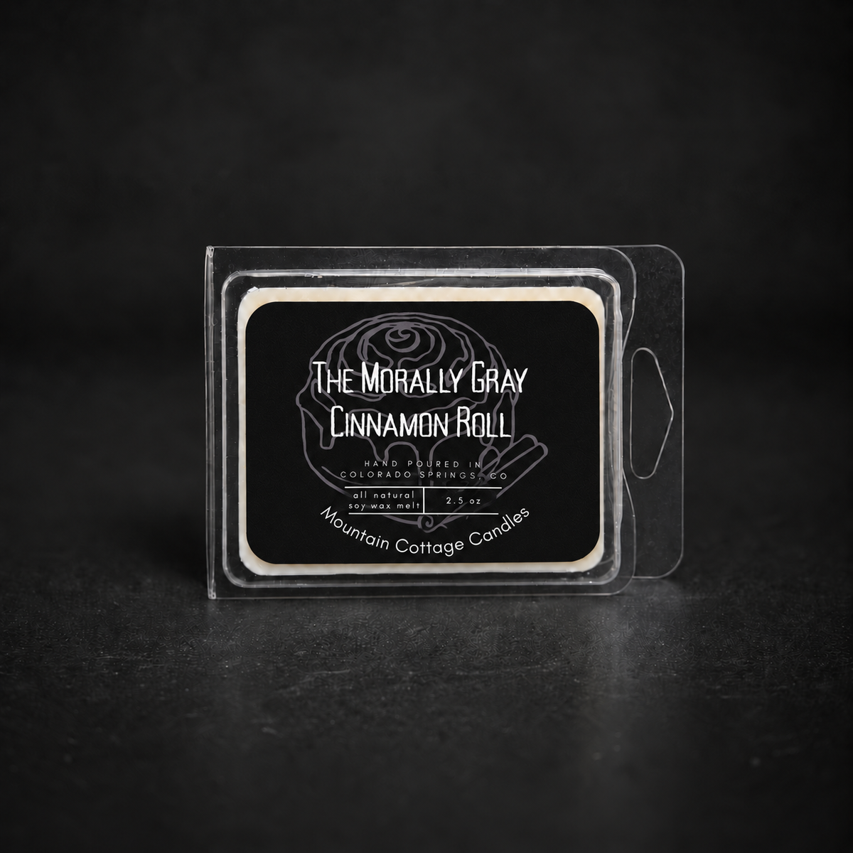 The Morally Gray Cinnamon Roll soy wax melt in a clamshell pack, black label drawn with an iced cinnamon roll and cinnamon sticks