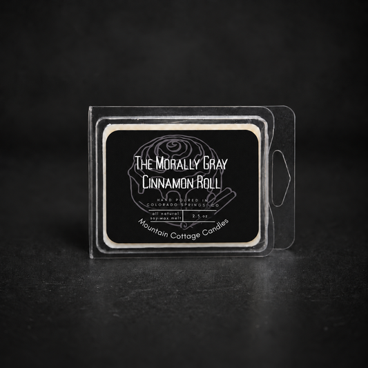 The Morally Gray Cinnamon Roll soy wax melt in a clamshell pack, black label drawn with an iced cinnamon roll and cinnamon sticks