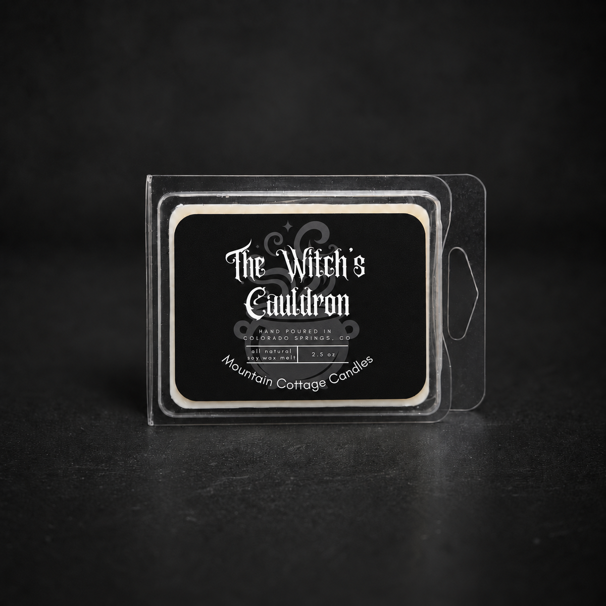 The Witch's Cauldron soy wax melt in a clear clamshell pack, black label with ornate scrollwork and sparkles