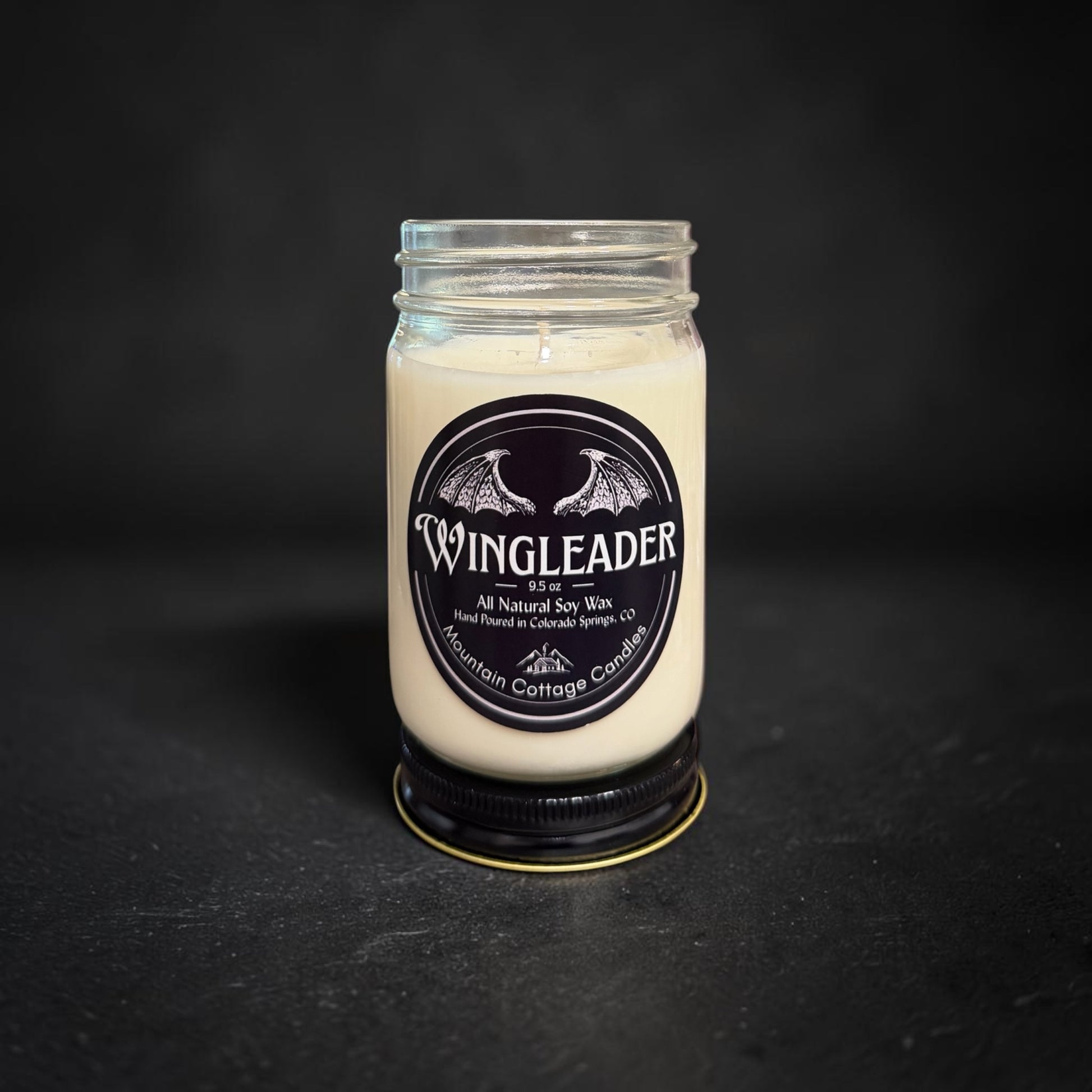 Wingleader soy candle in a clear glass jar with a black lid, black label showing a pair of outspread dragon wings